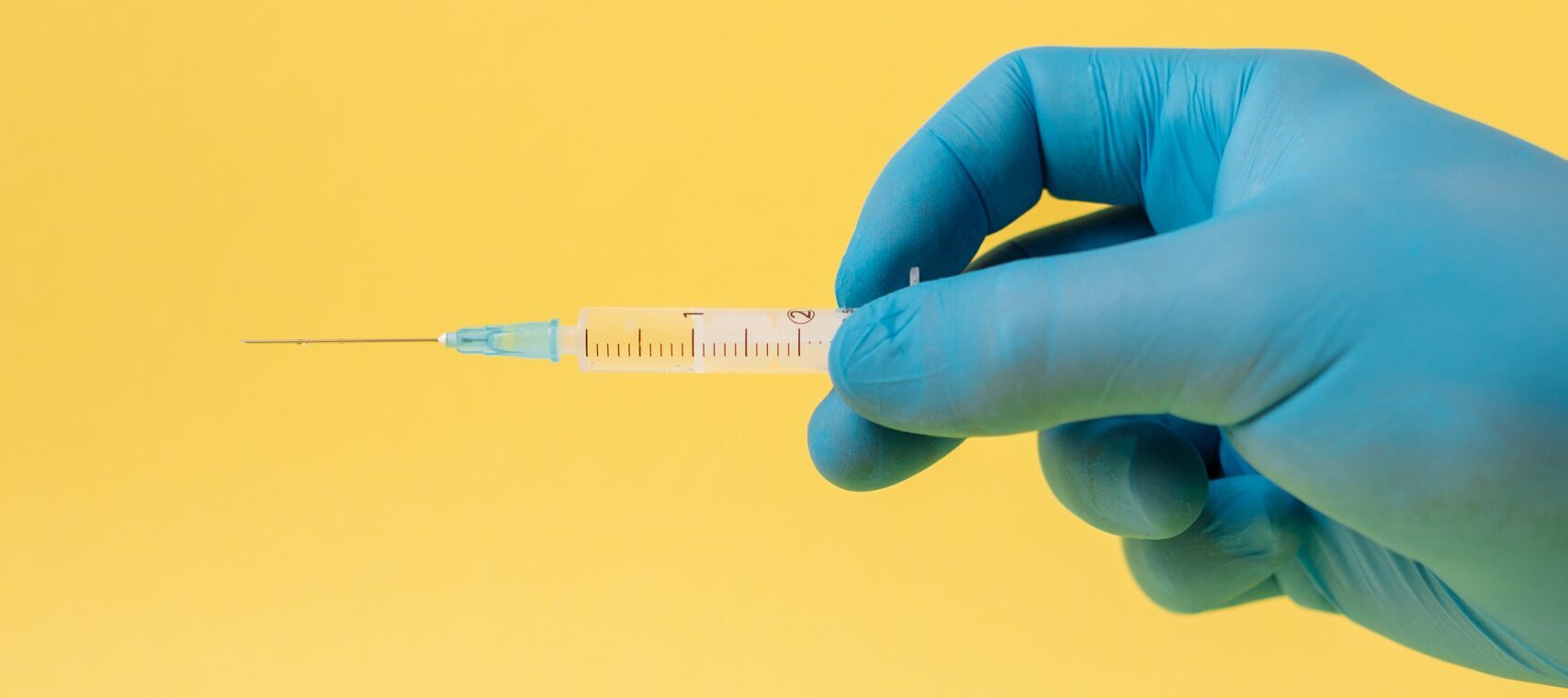 Hand wearing blue latex glove holding a filled syringe horizontally